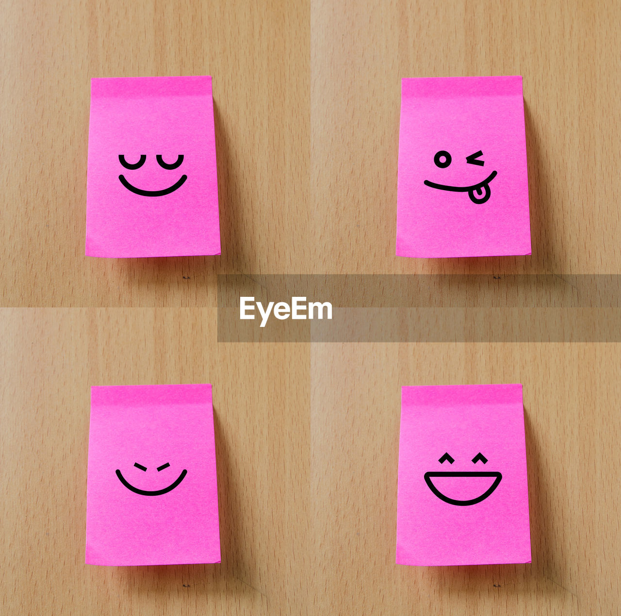 Close-up of smiley faces on pink adhesive notes over wooden table