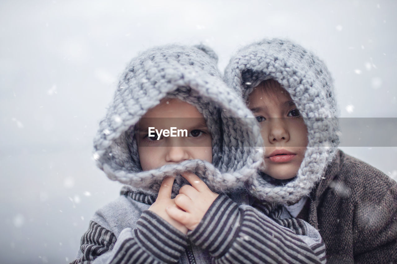 Girl in knitted grey hat hugging her frozen smaller brother