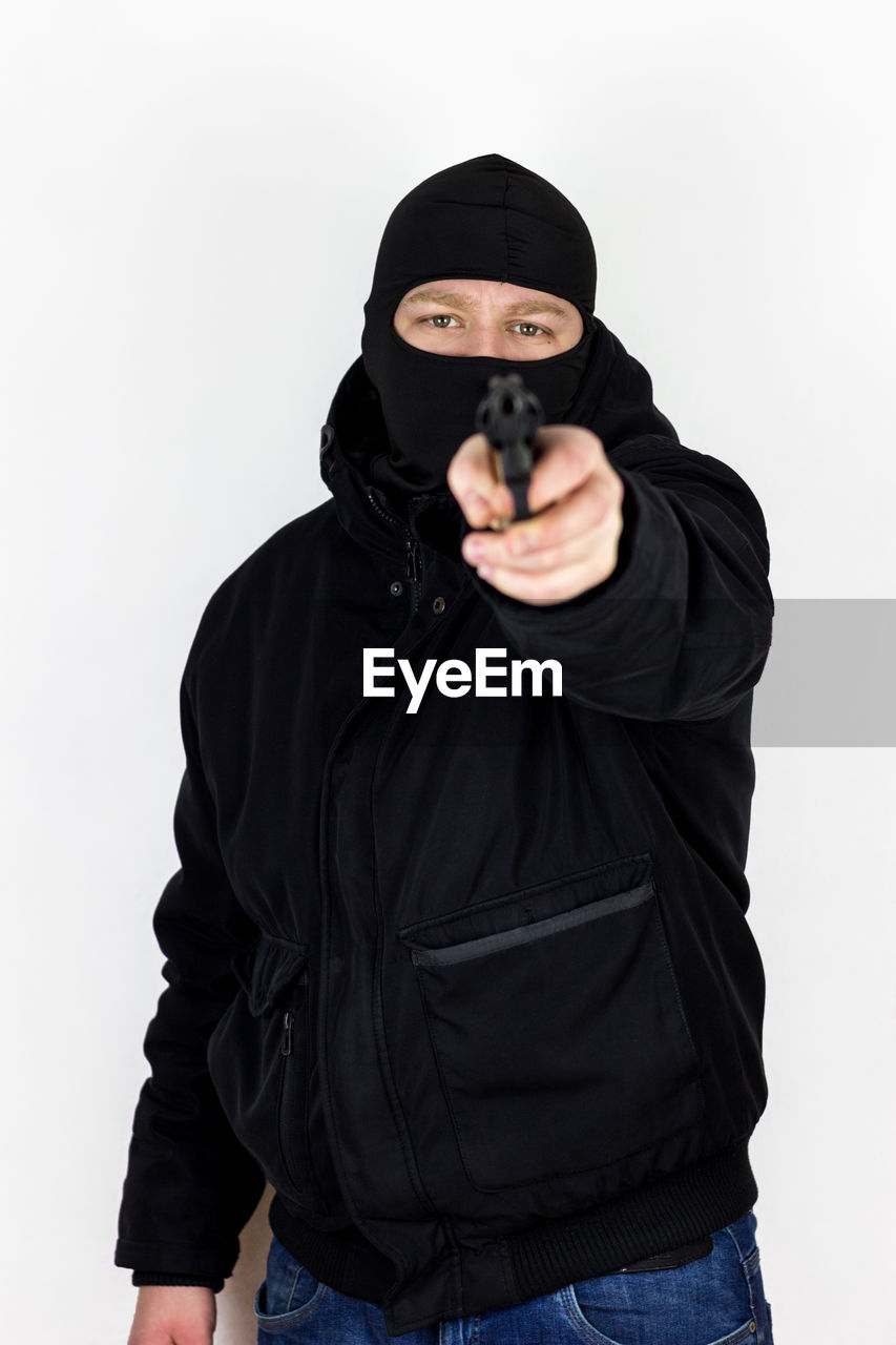 Portrait of robber aiming gun while standing on white background