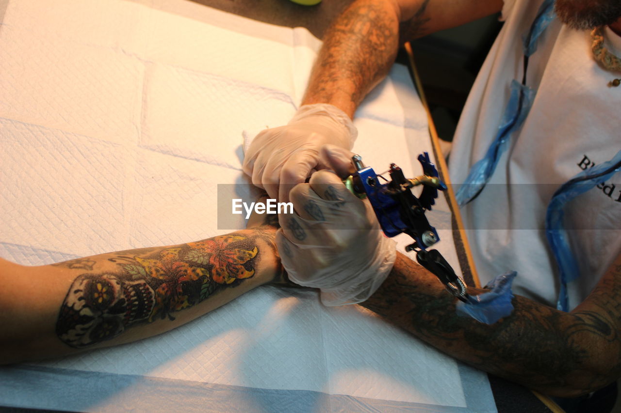 High angle view of artist making tattoo on hand