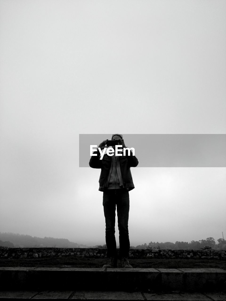 Man photographing through mobile phone while standing on steps against sky