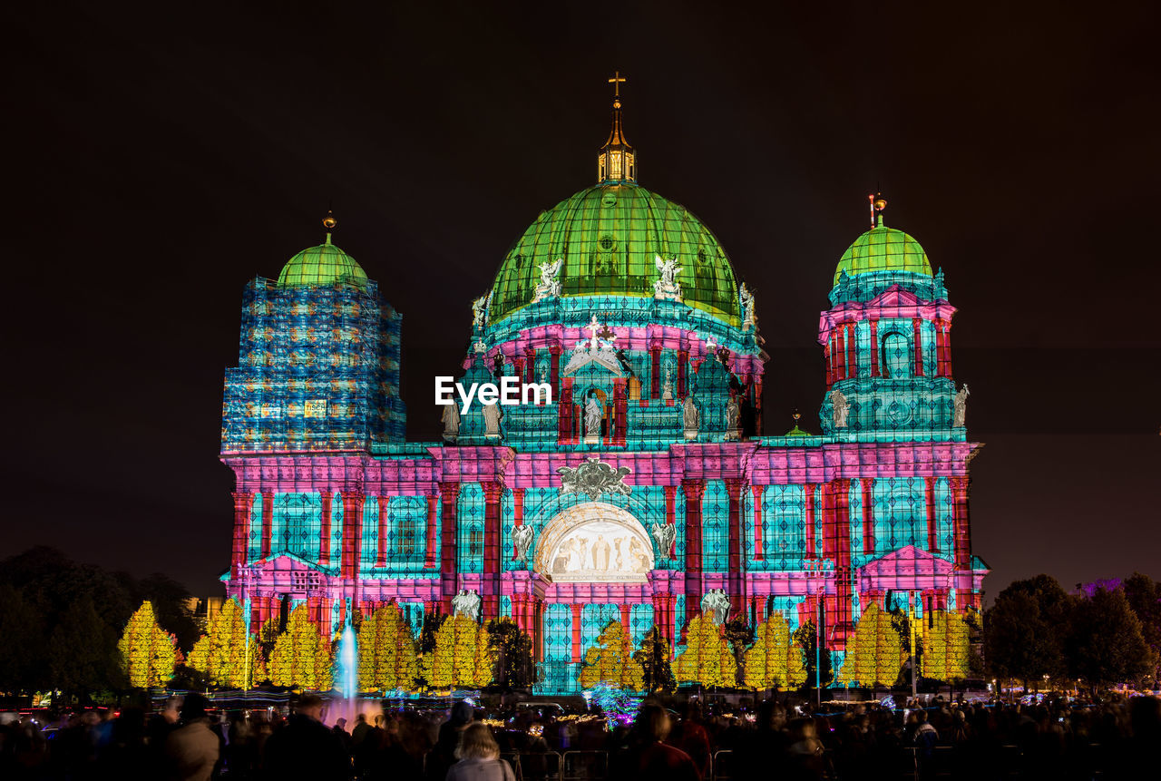 CROWD AT ILLUMINATED BUILDING AGAINST SKY