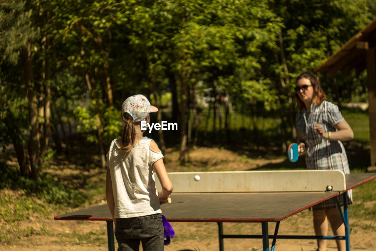 Mother and daughter playing table tennis at park during sunny day