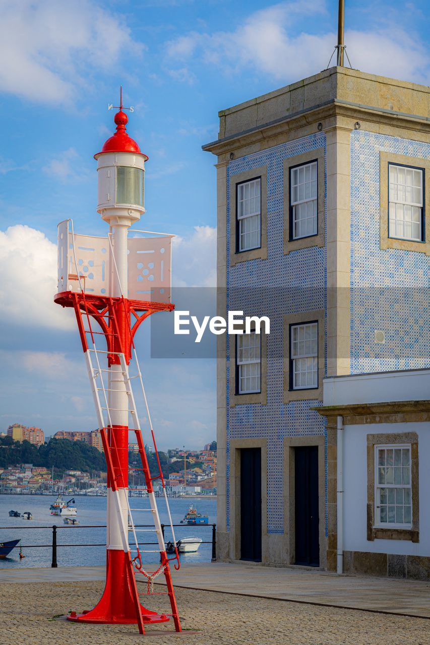 RED LIGHTHOUSE BY BUILDING AGAINST SKY