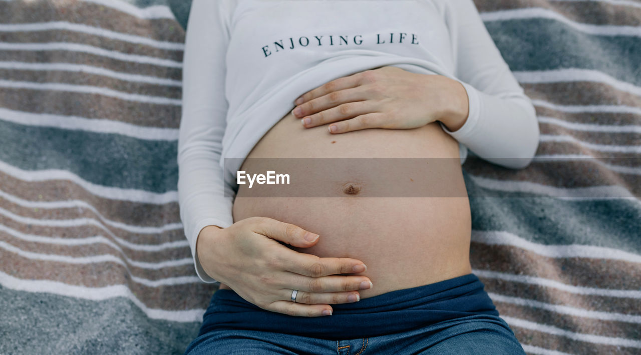 Midsection of pregnant woman touching abdomen while lying on blanket