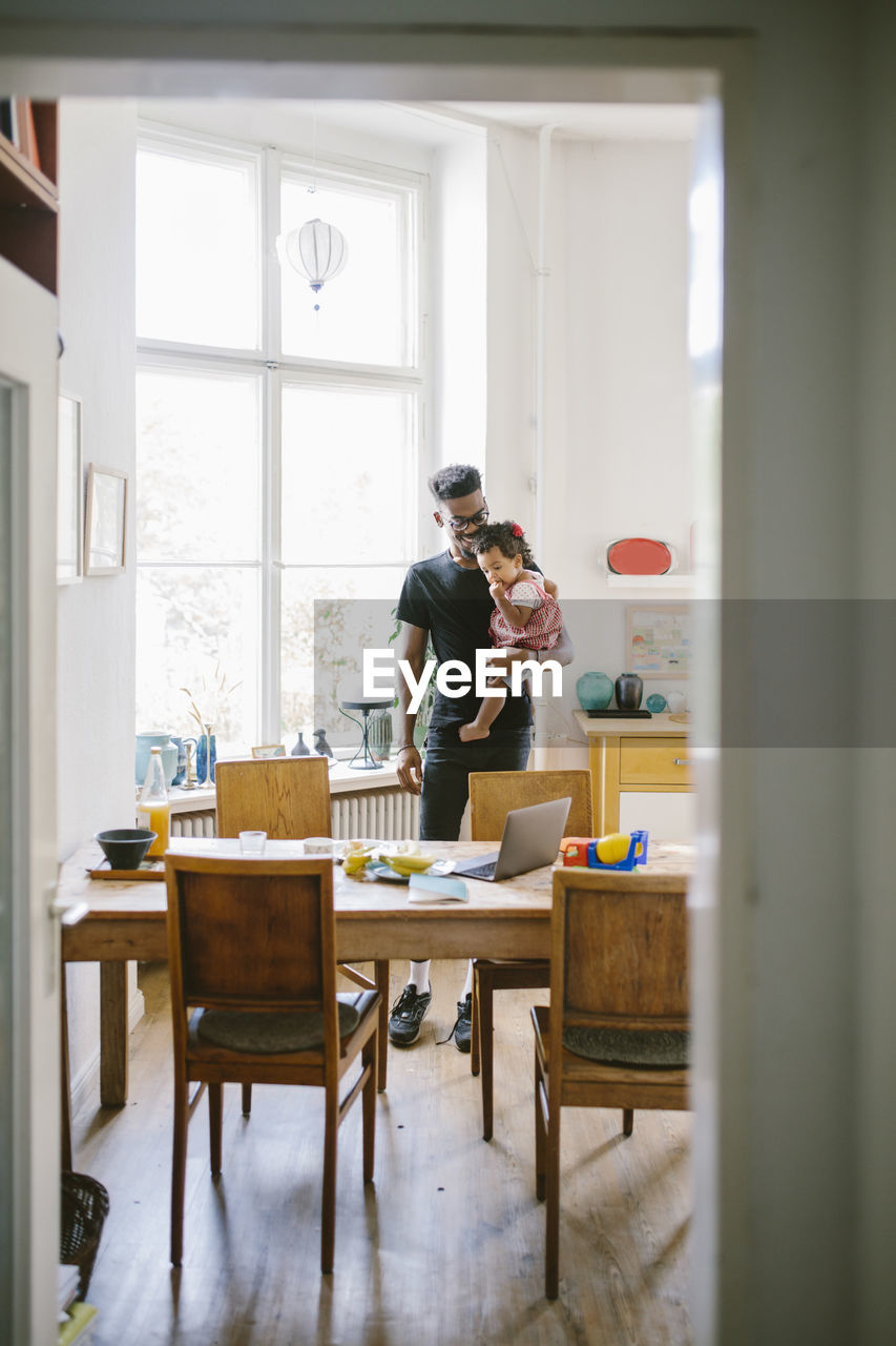 Young man carrying daughter seen through doorway at home