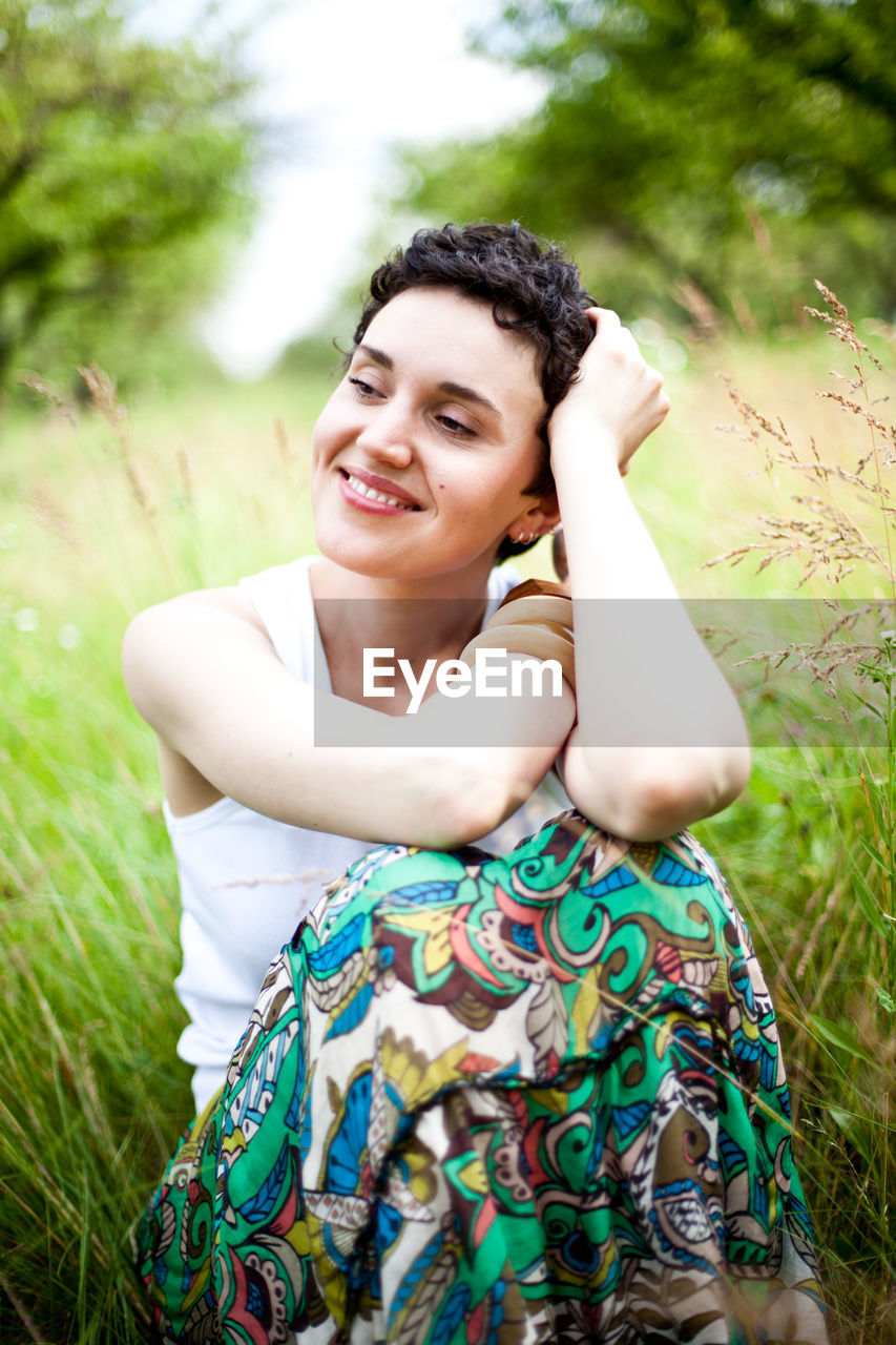 Smiling woman looking away while sitting on field