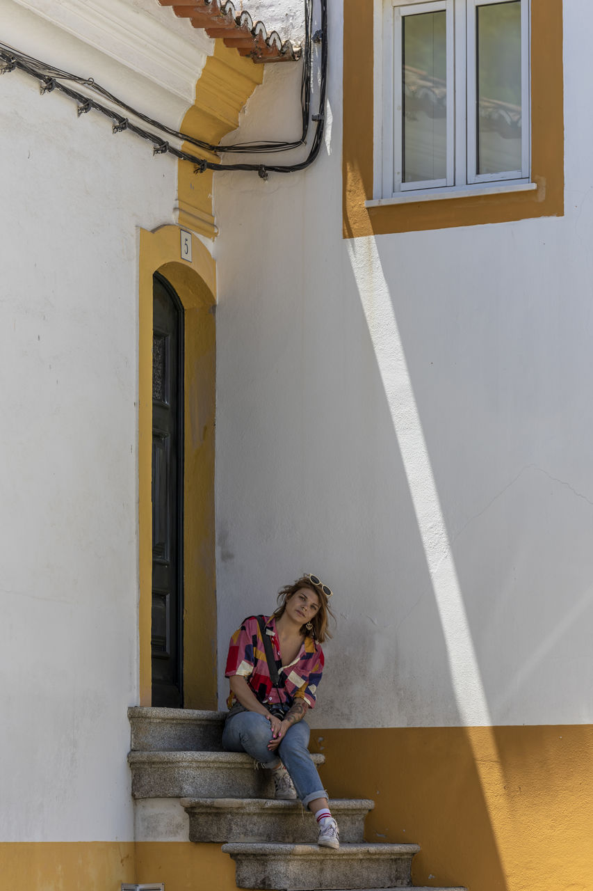 WOMAN SITTING BY BUILDING