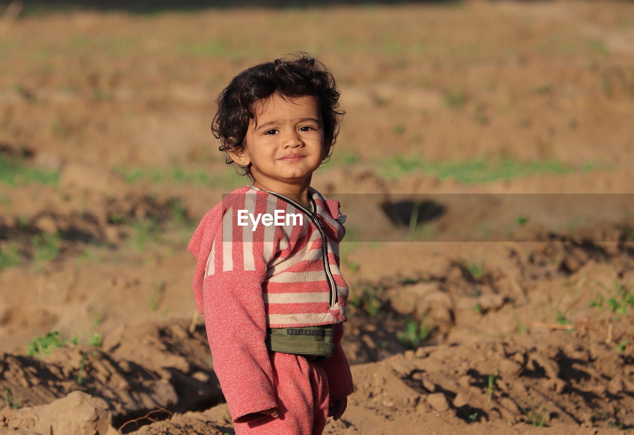 A closeup portrait photo of beautiful hindu little male boy standing in garden at sunset. 