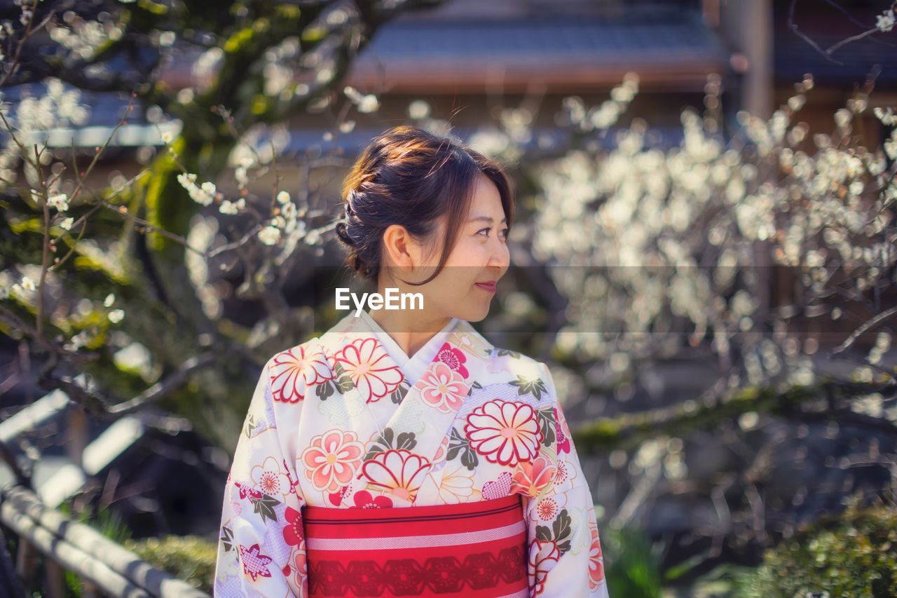 Smiling beautiful woman in traditional cloths standing against cherry trees