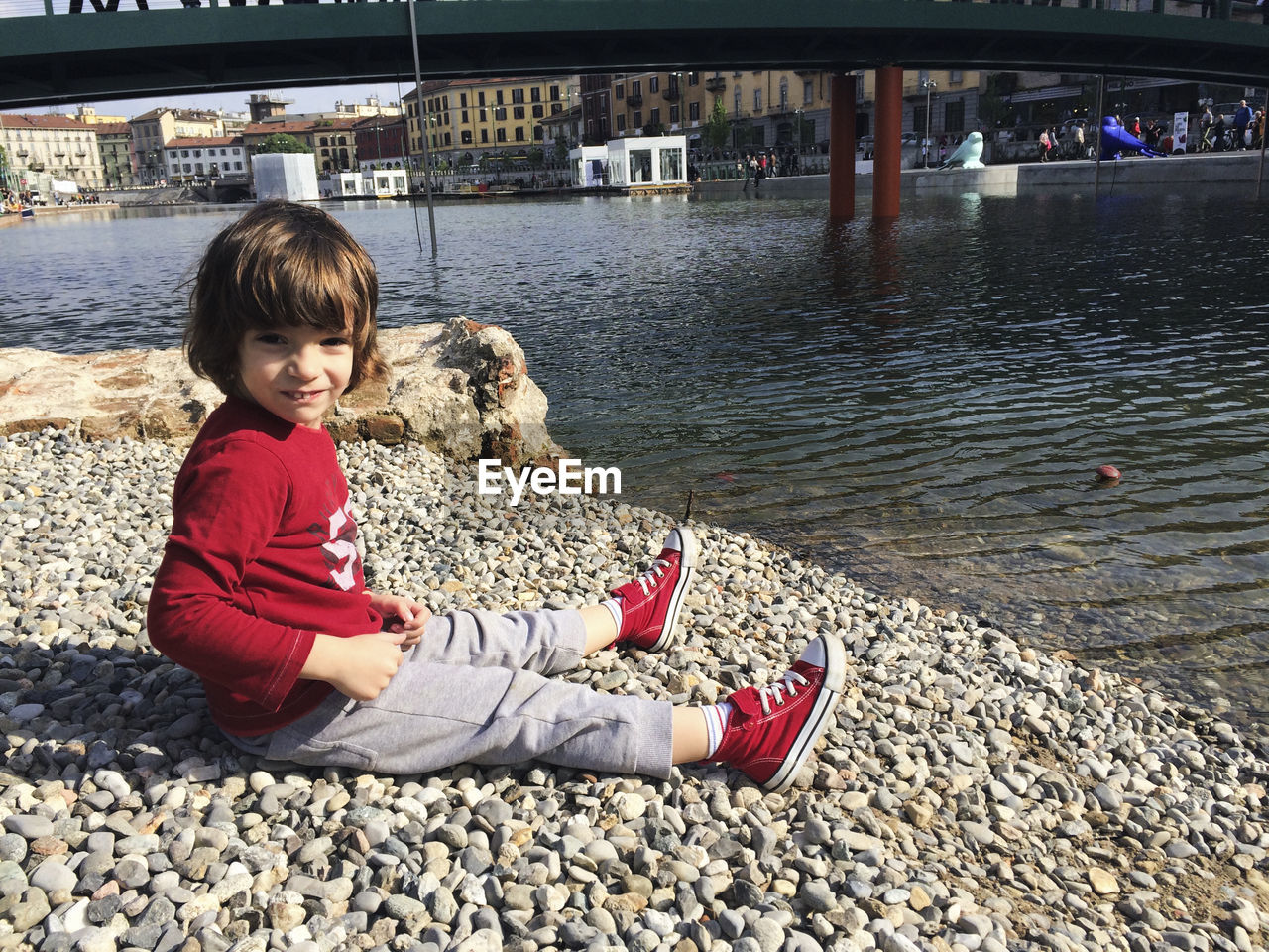 Portrait of cute boy sitting at lakeshore in city