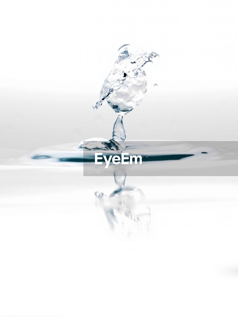 Close-up of drop splashing on water against white background