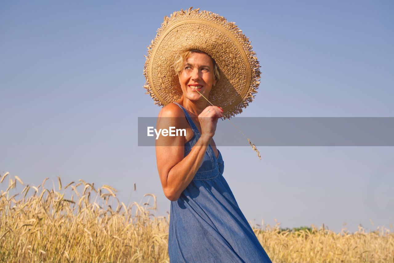 Side view of woman wearing hat standing on land against clear sky