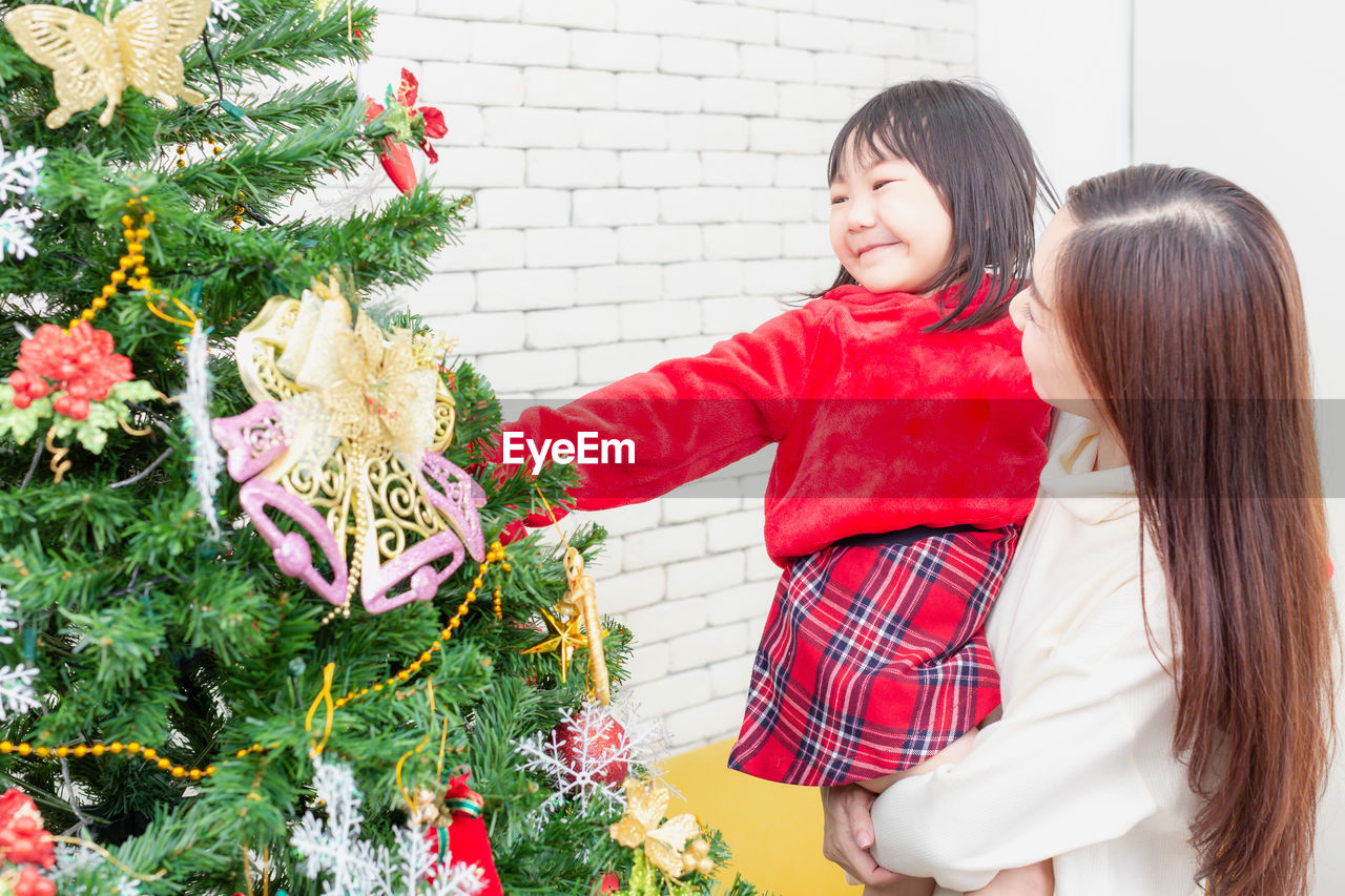 Happy new year. asian girls wearing red dresses are decorating christmas trees. mother and daughter.