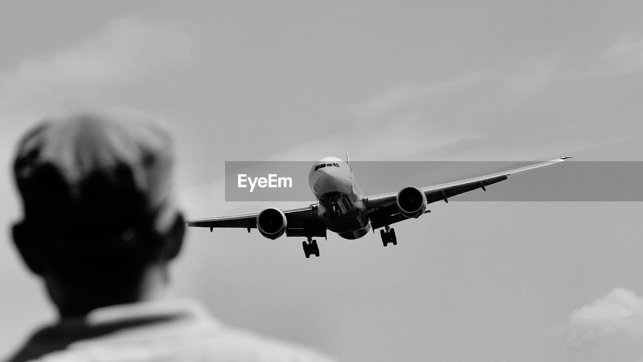 Rear view of person watching airplane flying against the sky
