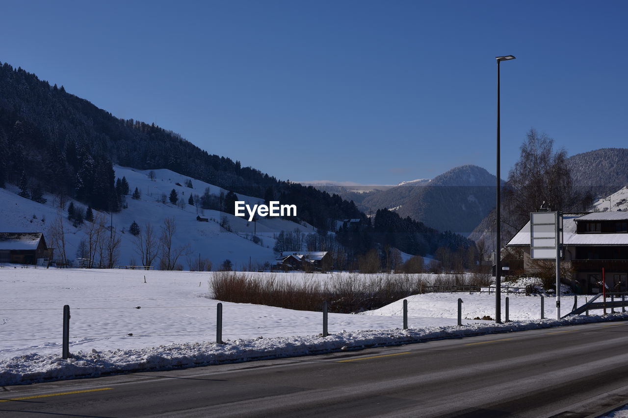 Road by mountains against clear sky during winter