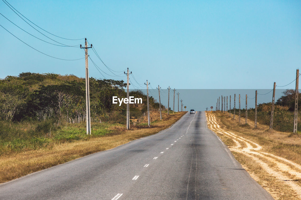 Road by electricity pylons against clear sky