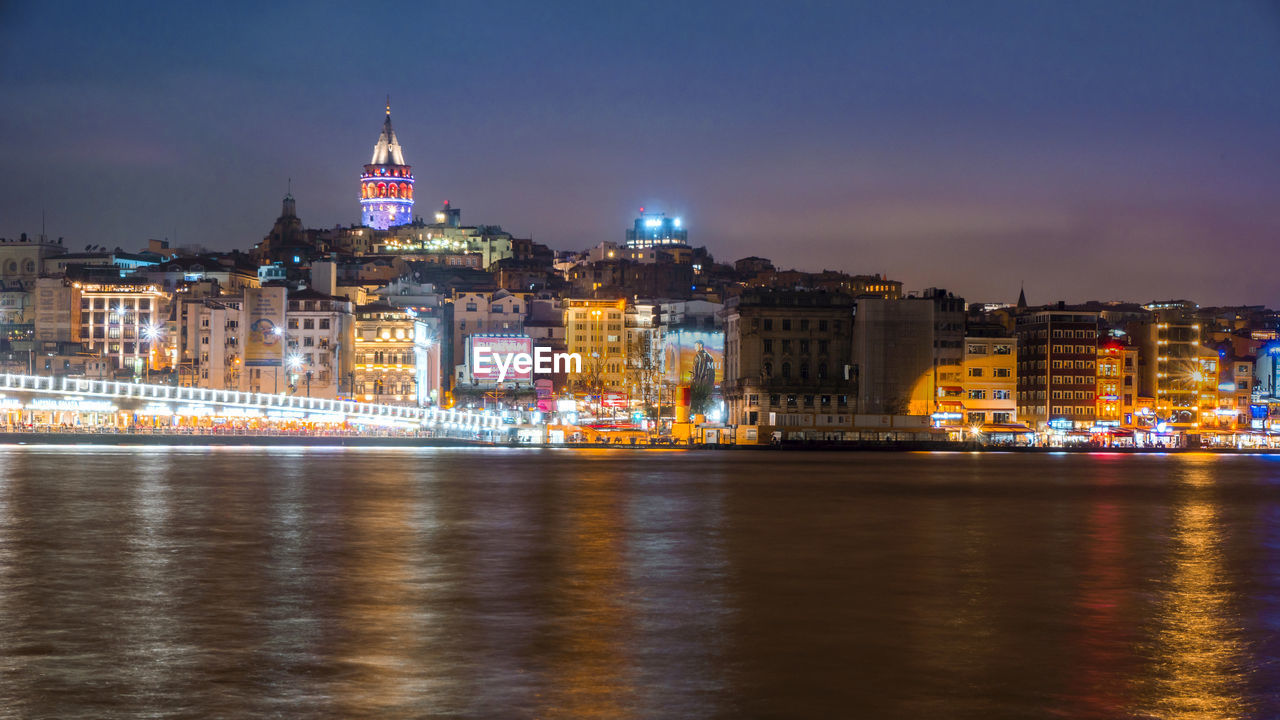 ILLUMINATED CITY BUILDINGS AT WATERFRONT