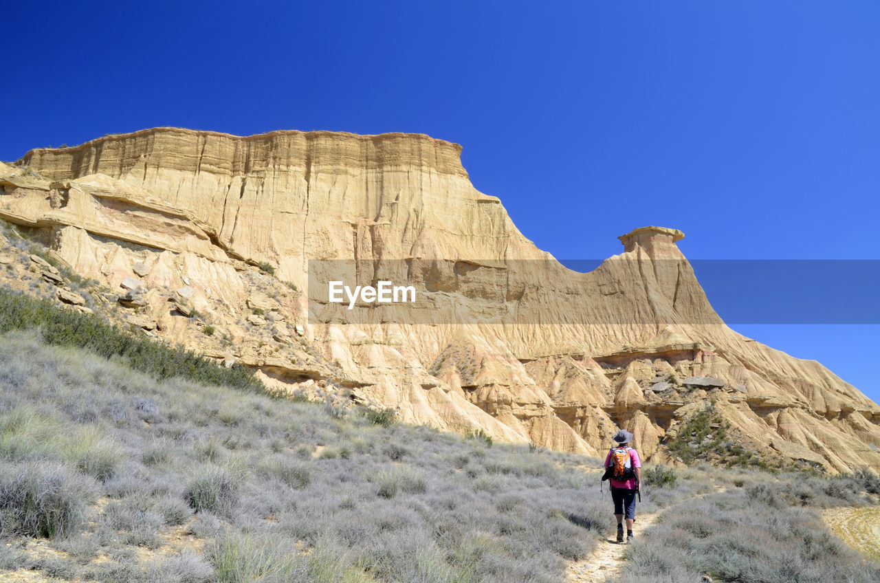 REAR VIEW OF MAN ON ROCK AGAINST SKY