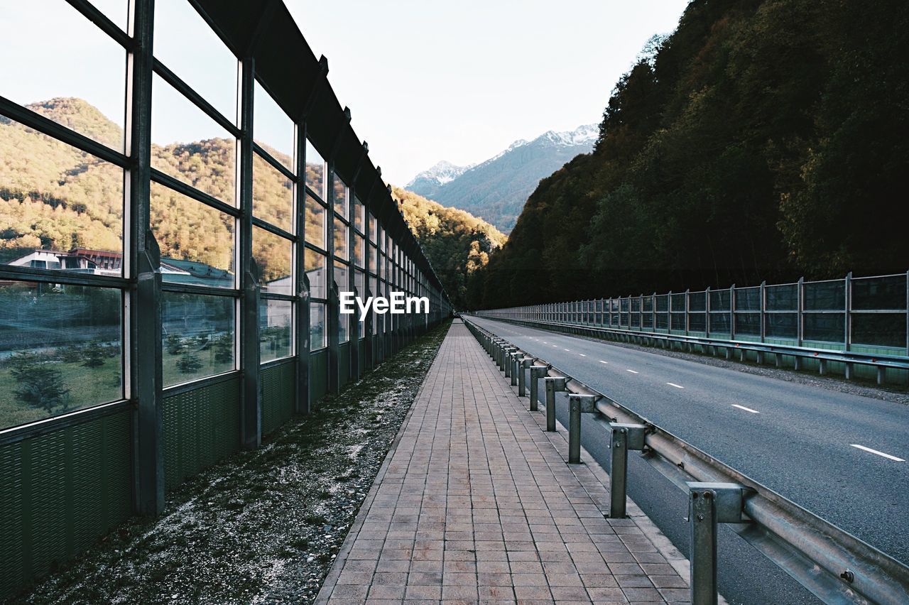 Sidewalk leading towards mountains against clear sky