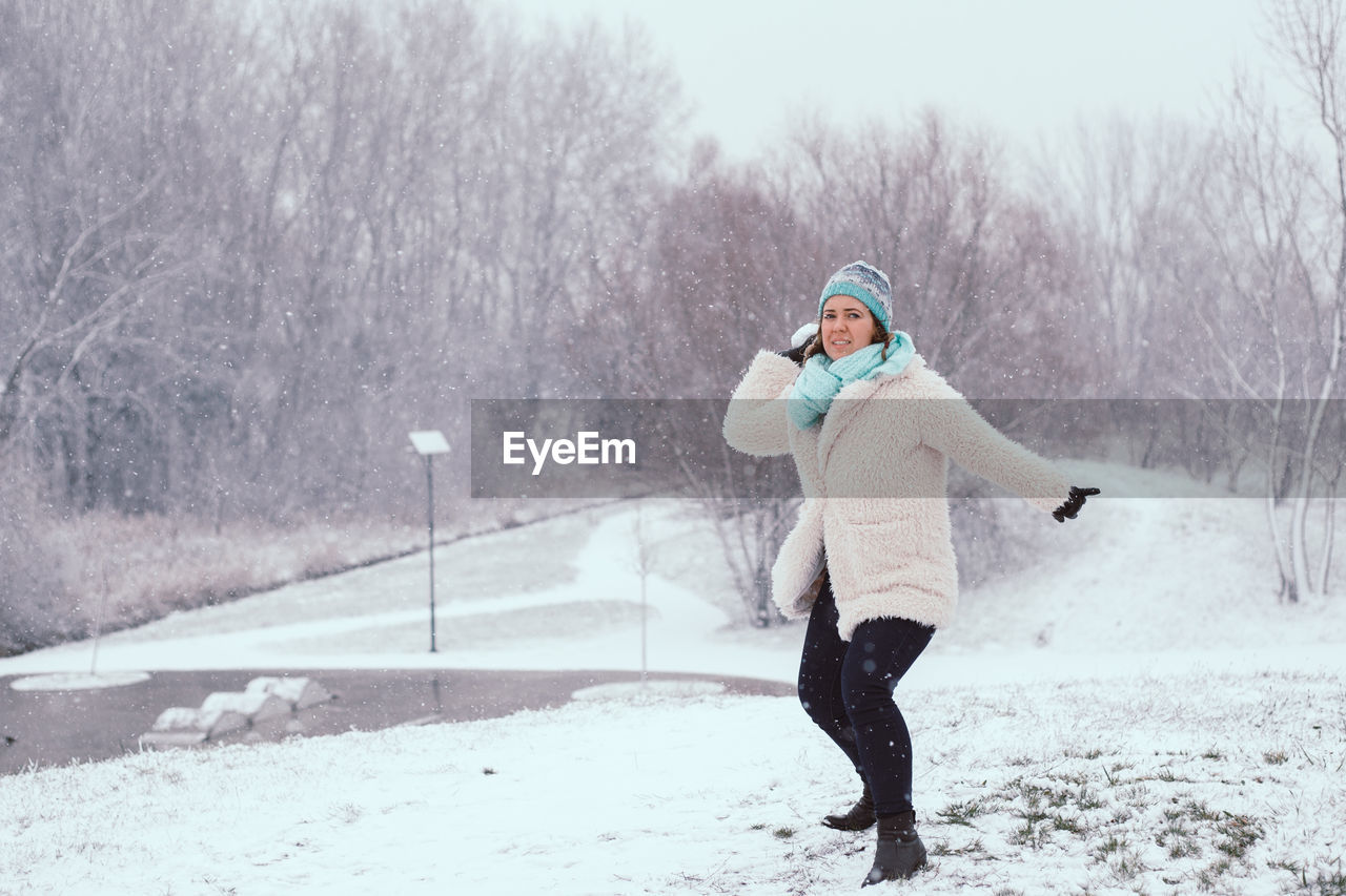 Portrait of young woman playing with snow at park during winter