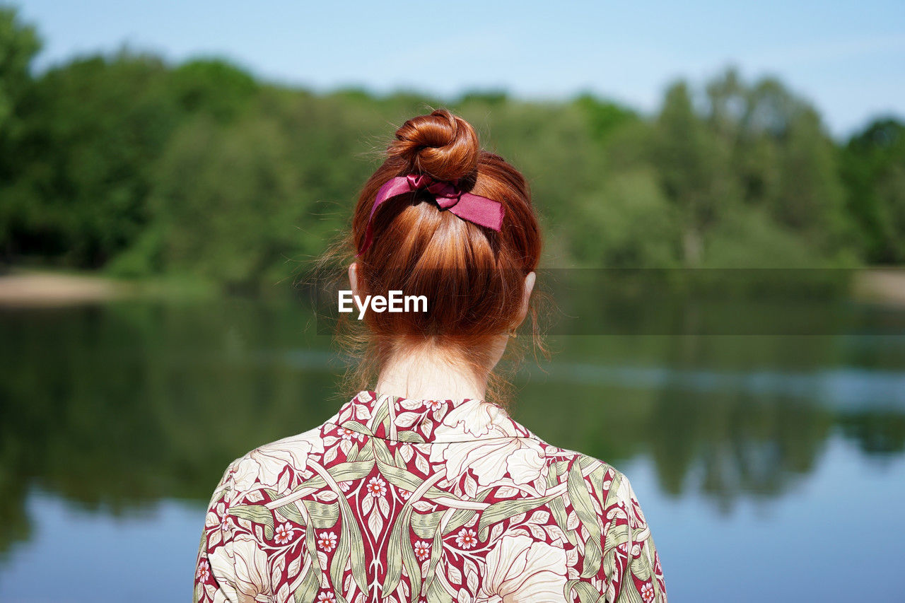 Back view of woman with red hair bun looking at lake