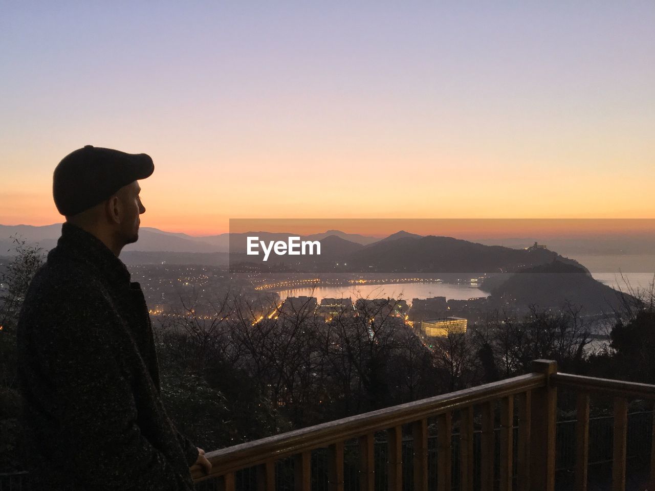 Man looking at scenic view from balcony against sky during sunset