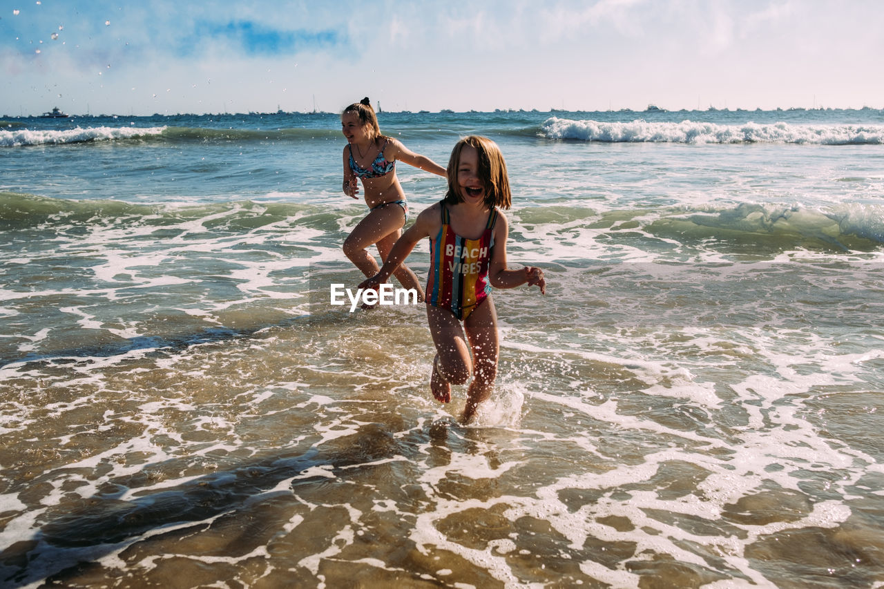 Siblings running in water at beach on a sunny day
