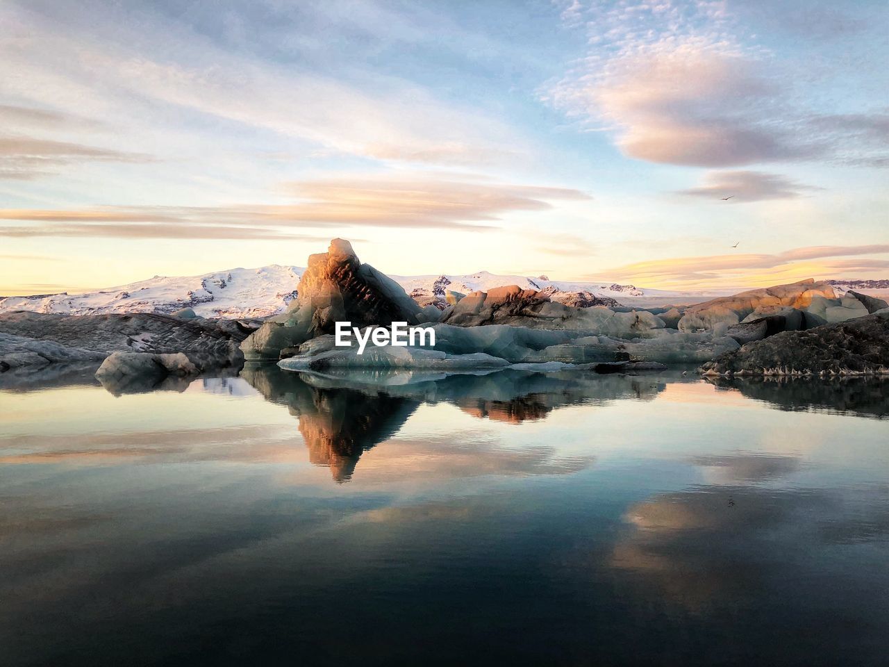 Reflection on snowy rocks in lake against sky