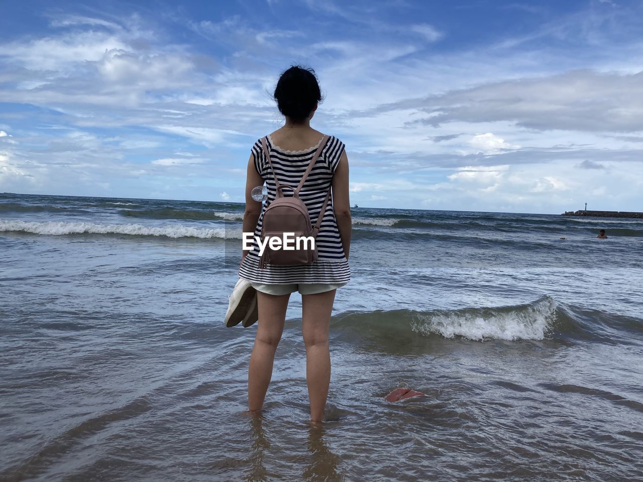 REAR VIEW OF WOMAN STANDING ON BEACH AGAINST SKY