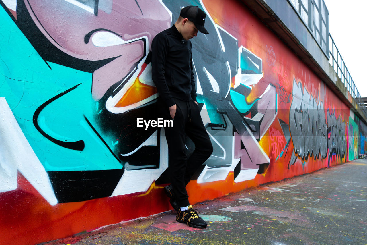 MAN STANDING ON GRAFFITI WALL