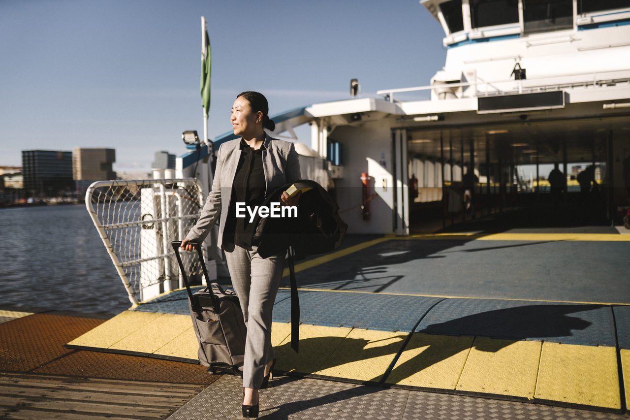 Businesswoman pulling wheeled luggage while disembarking from ferry on sunny day