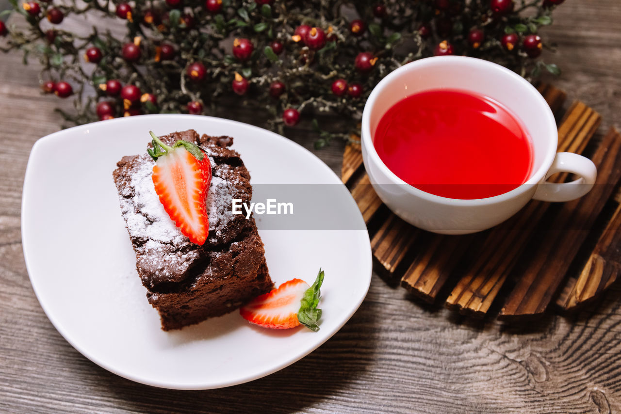 A portion of chocolate brownie and a cup of fruit tea to take time a have a break. on a wooden table