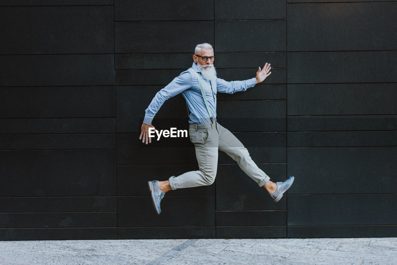 Senior hipster jumping against wall