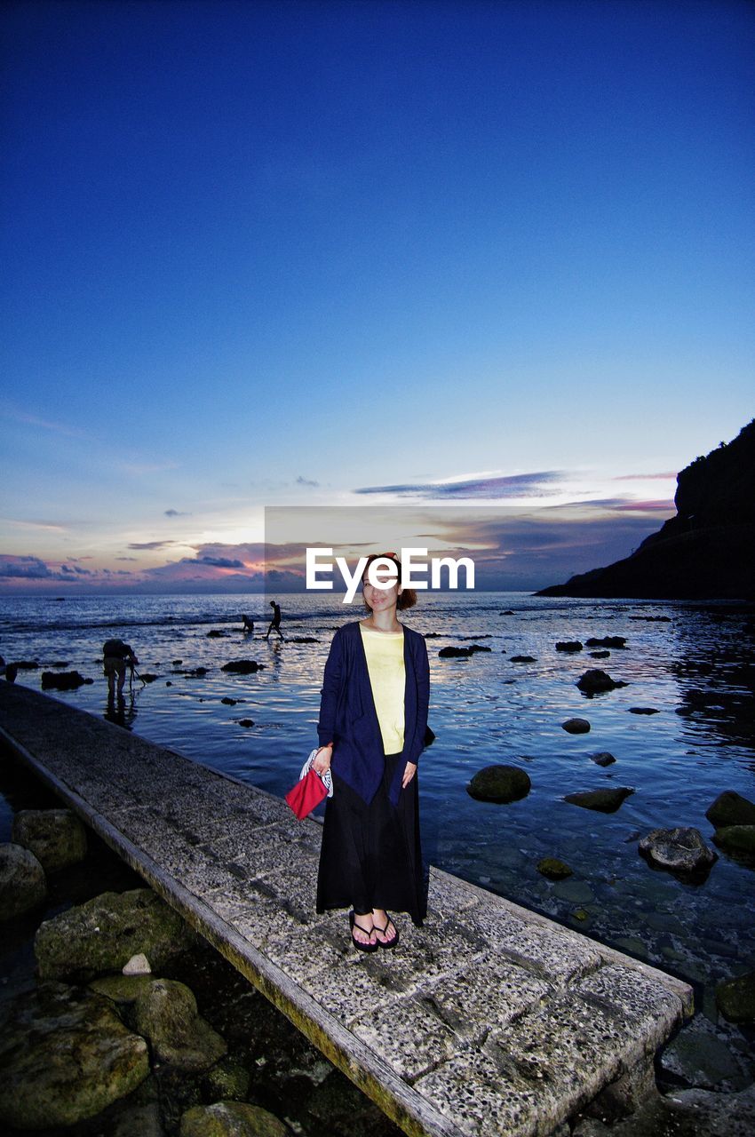 Young woman standing on pier over sea against sky during sunset