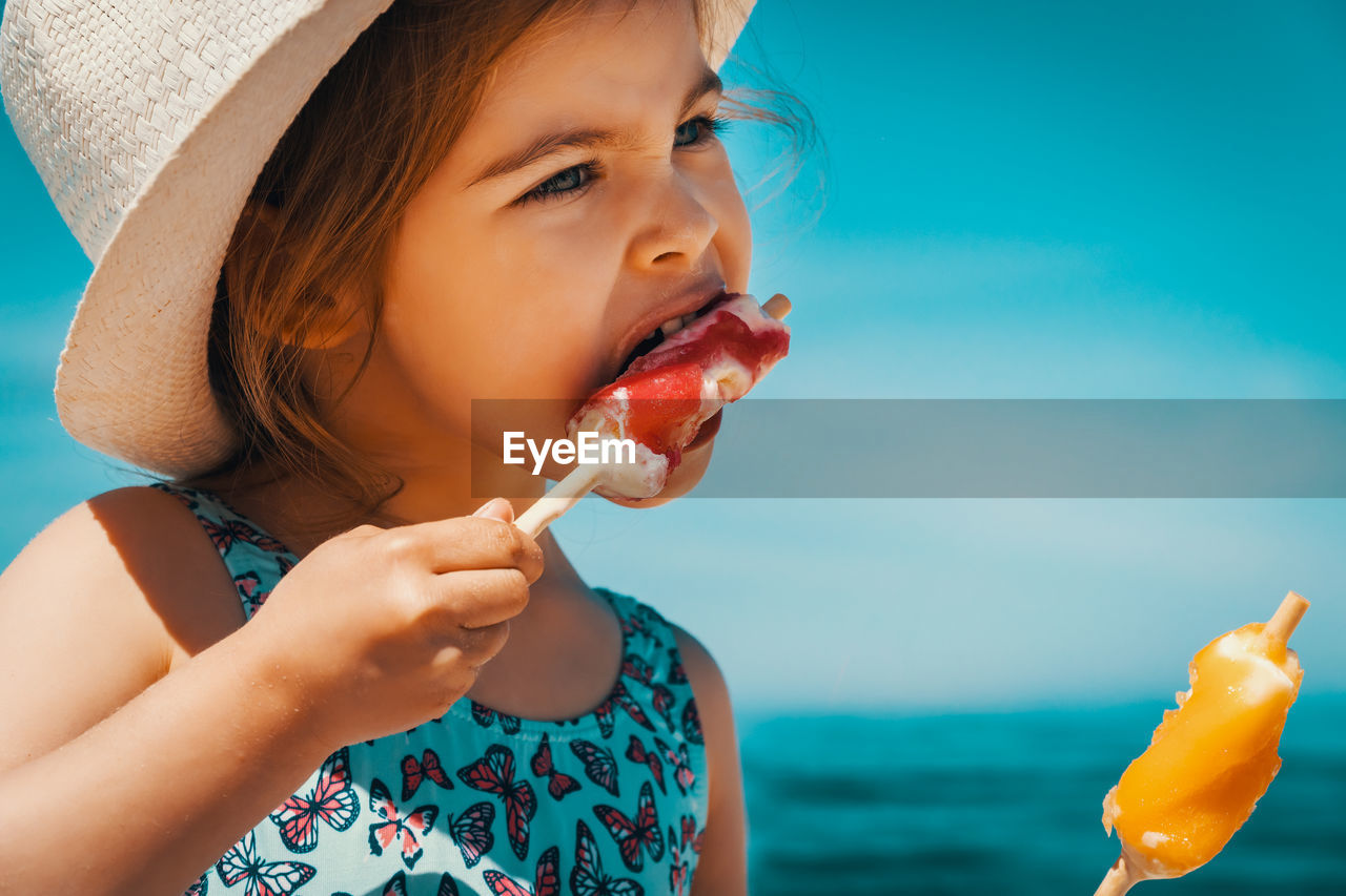 Cute girl looking away while eating ice cream at beach