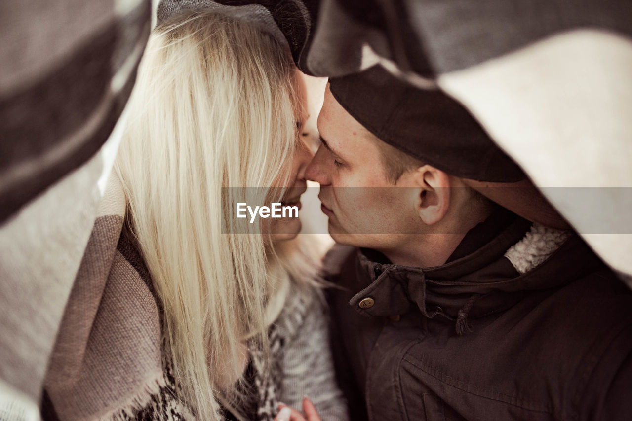 Close-up of couple kissing under blanket