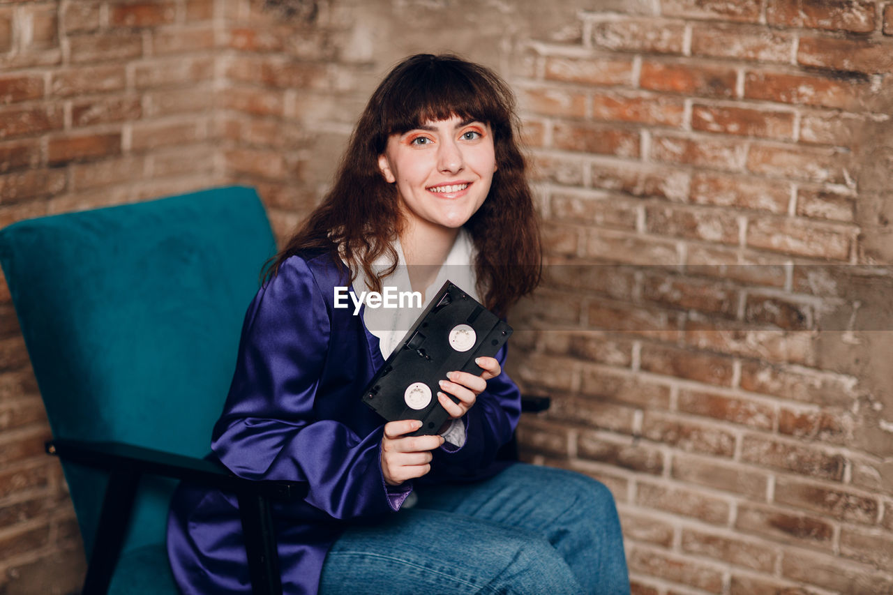 portrait of young woman sitting against brick wall