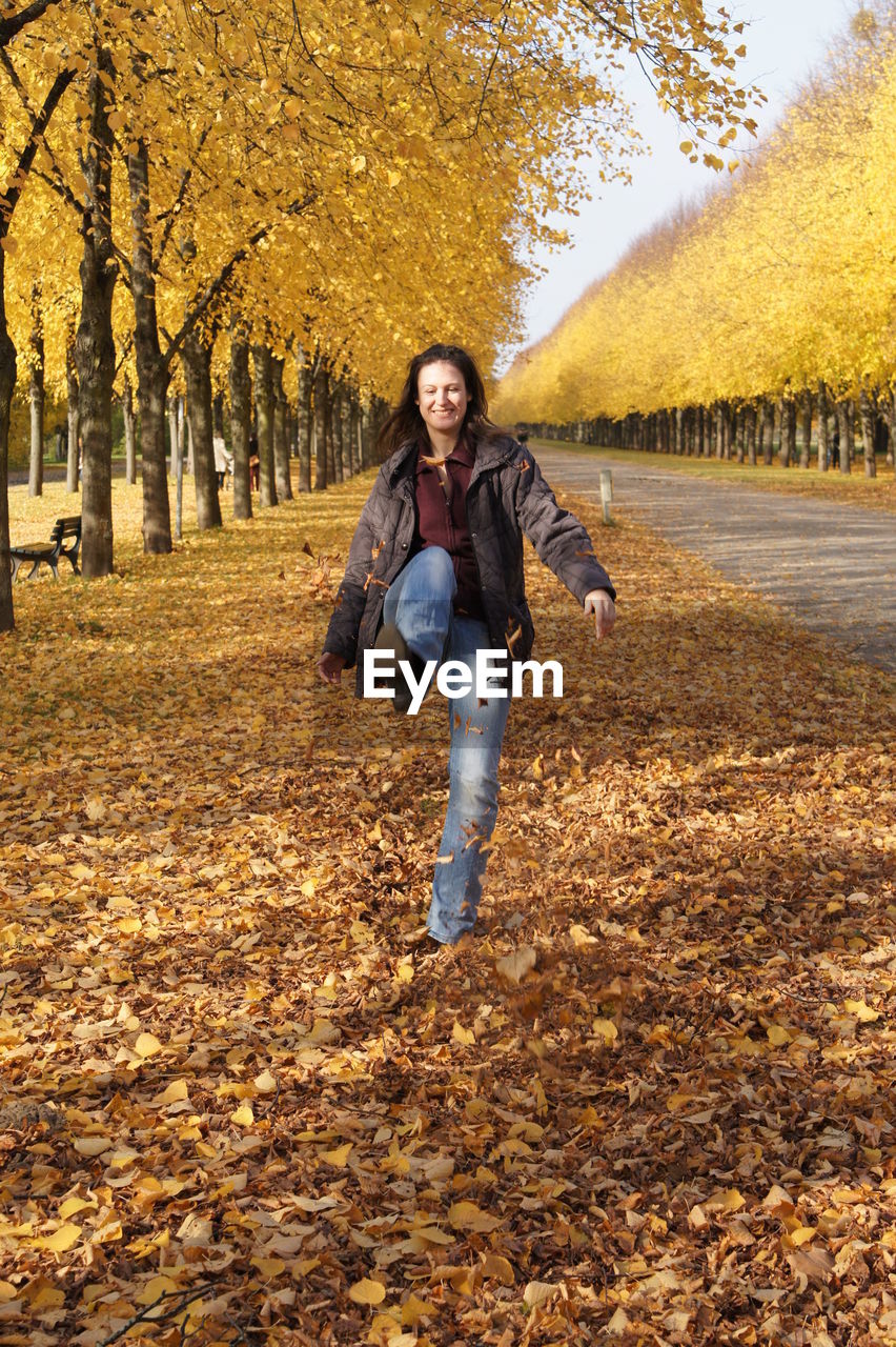 Young woman kicking autumn leaves on field by trees