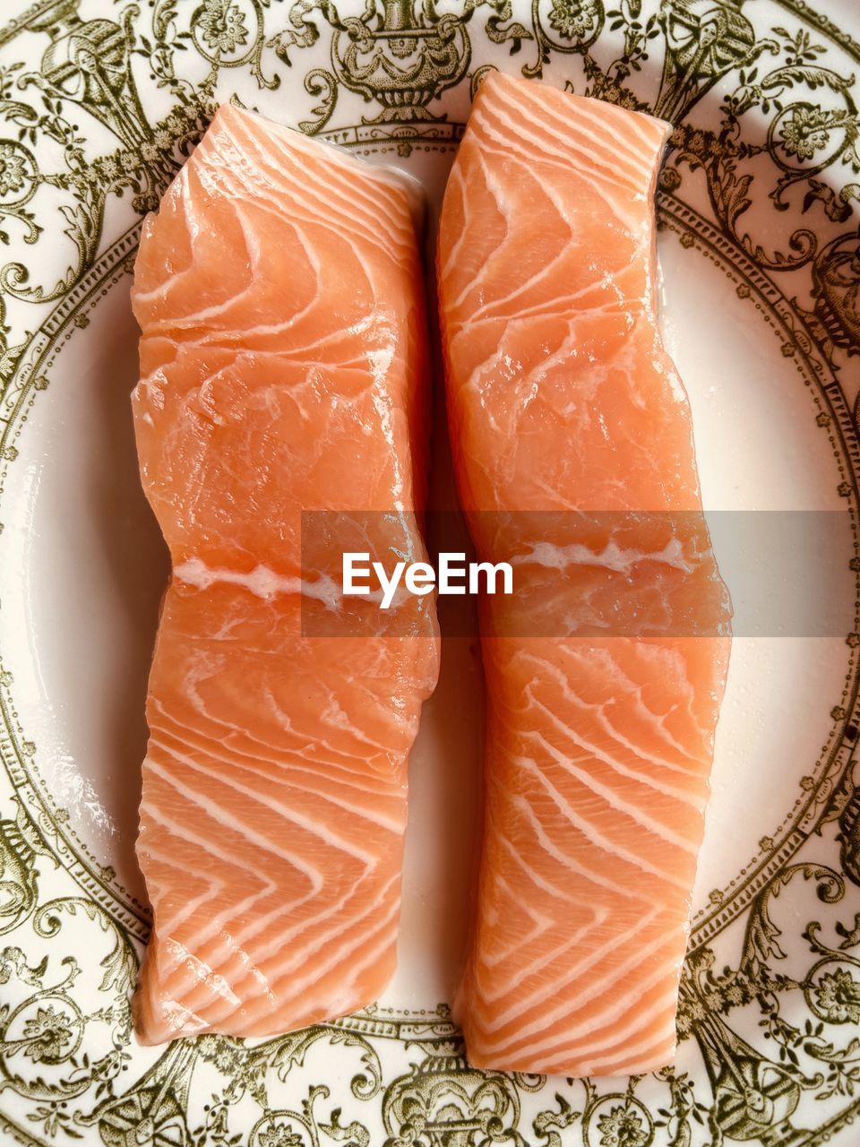 Close-up of two fresh salmon fillets. pinky orange fish. in an ornate green and white ceramic dish.