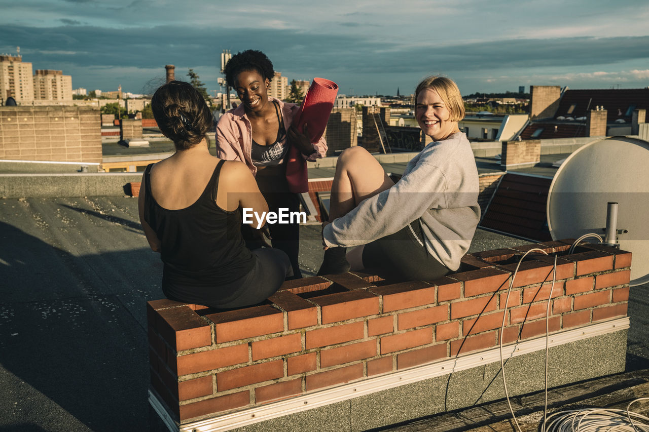 Portrait of smiling female friends after yoga on rooftop during sunrise