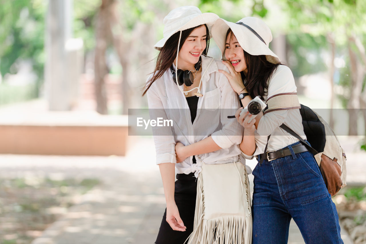 Women holding camera while standing against trees