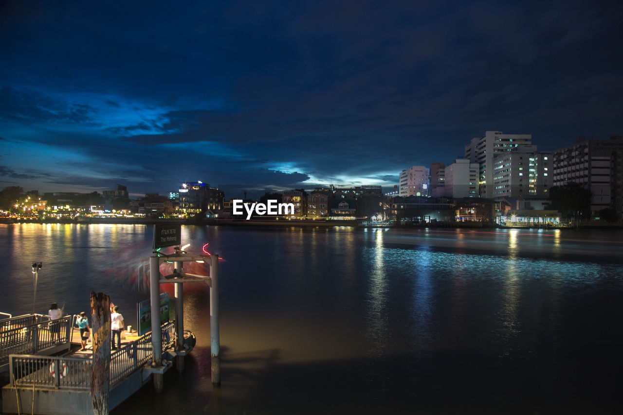 Illuminated city by river against sky at night