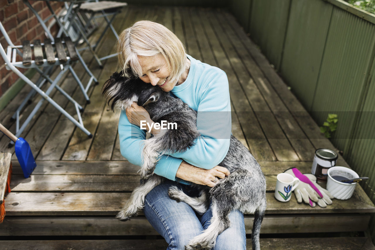 Happy senior woman embracing dog while sitting on porch