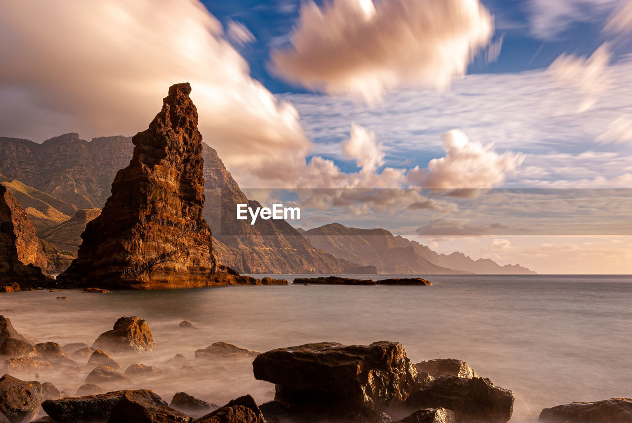 SCENIC VIEW OF ROCKS IN SEA AGAINST MOUNTAINS