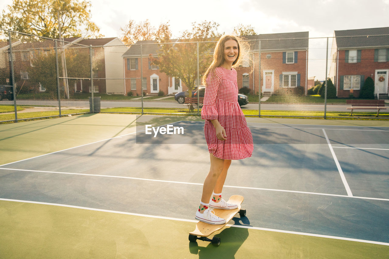 Smiling girl learning how to skateboard on a tennis court with sunlight on her hair