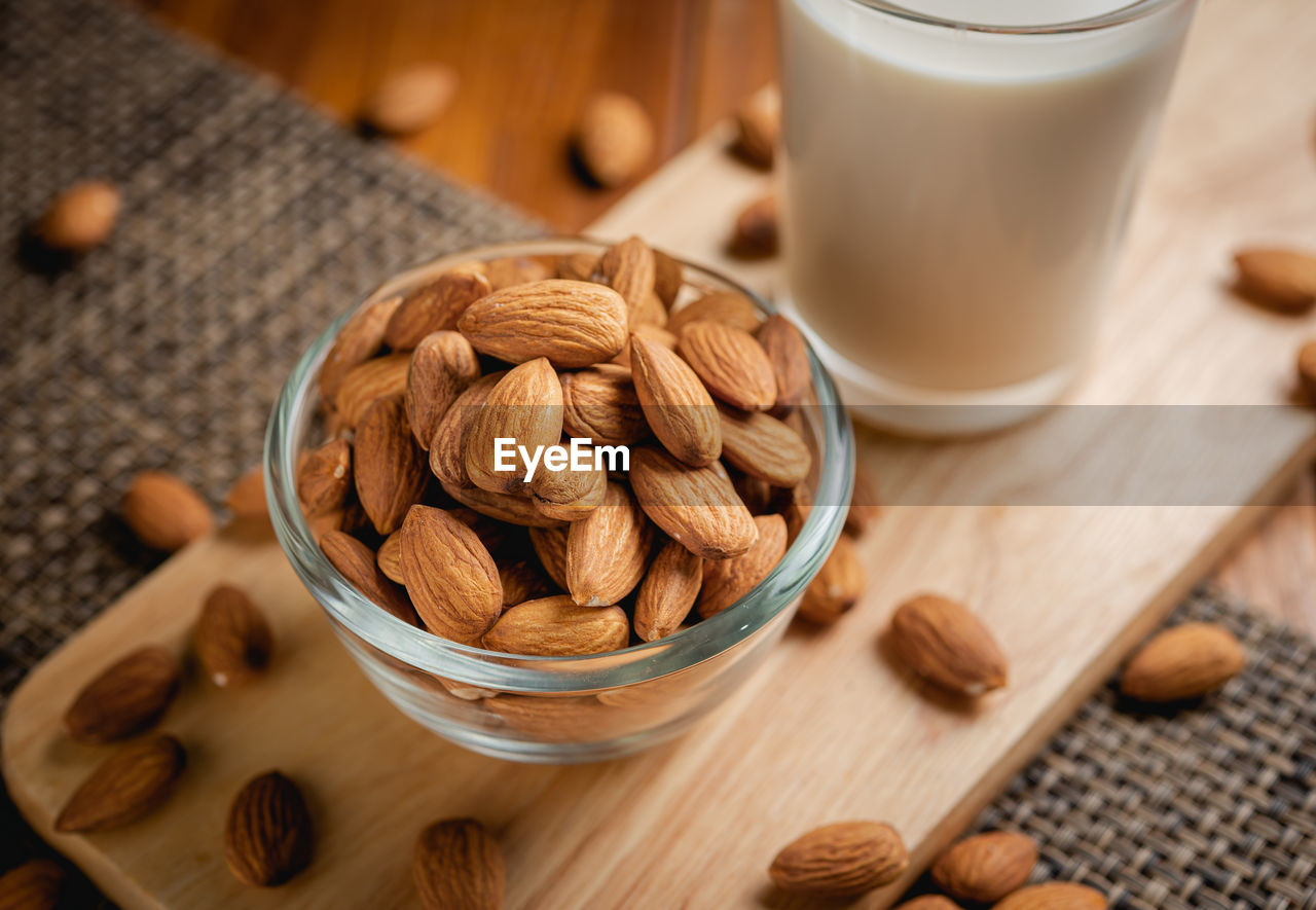 Almond milk in the glass with almond in the glass bowl on the wooden table.