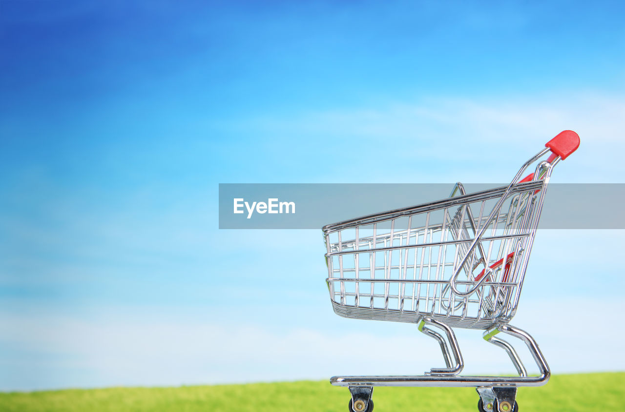 Shopping cart on field against sky