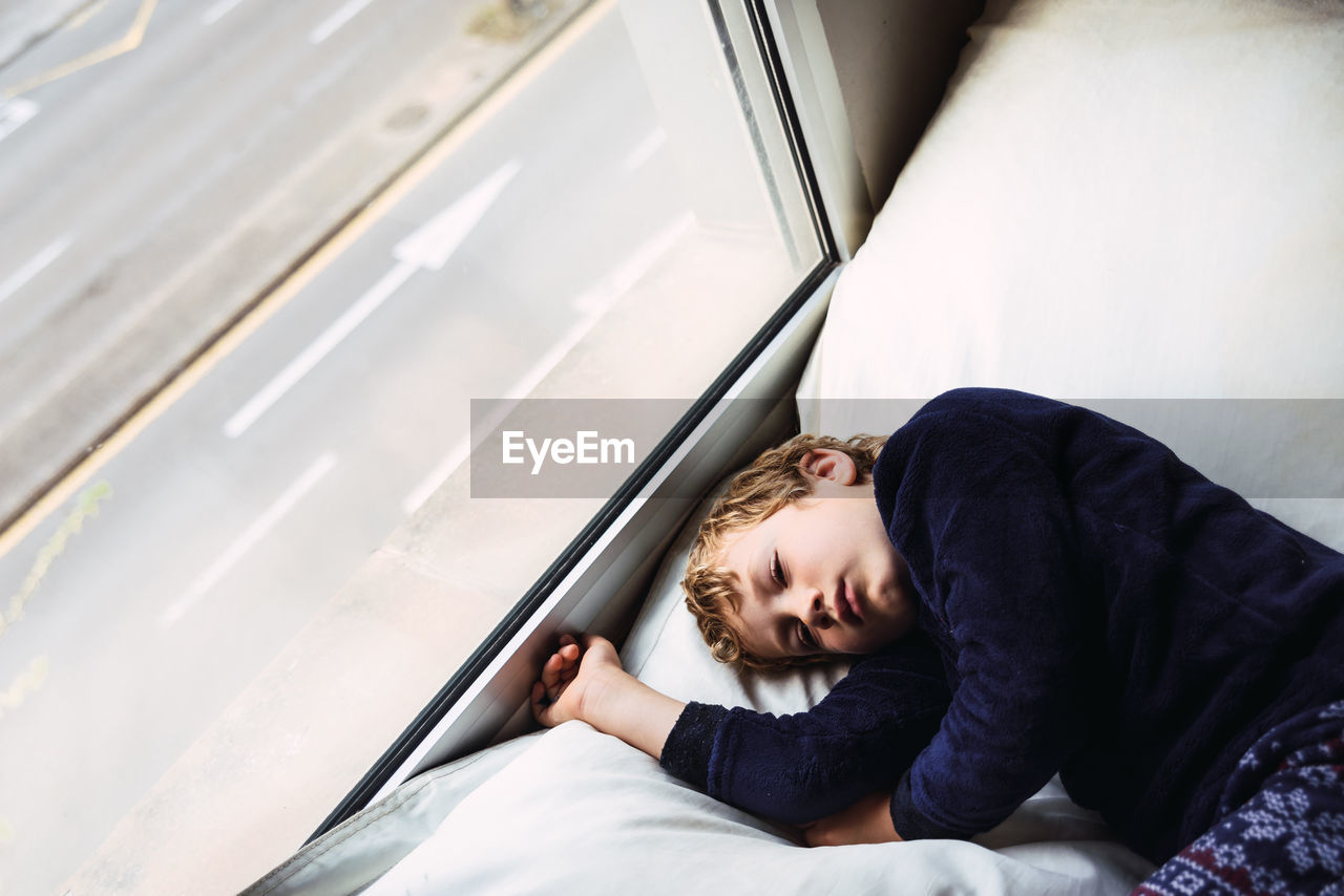 High angle view of boy sleeping on bed by window