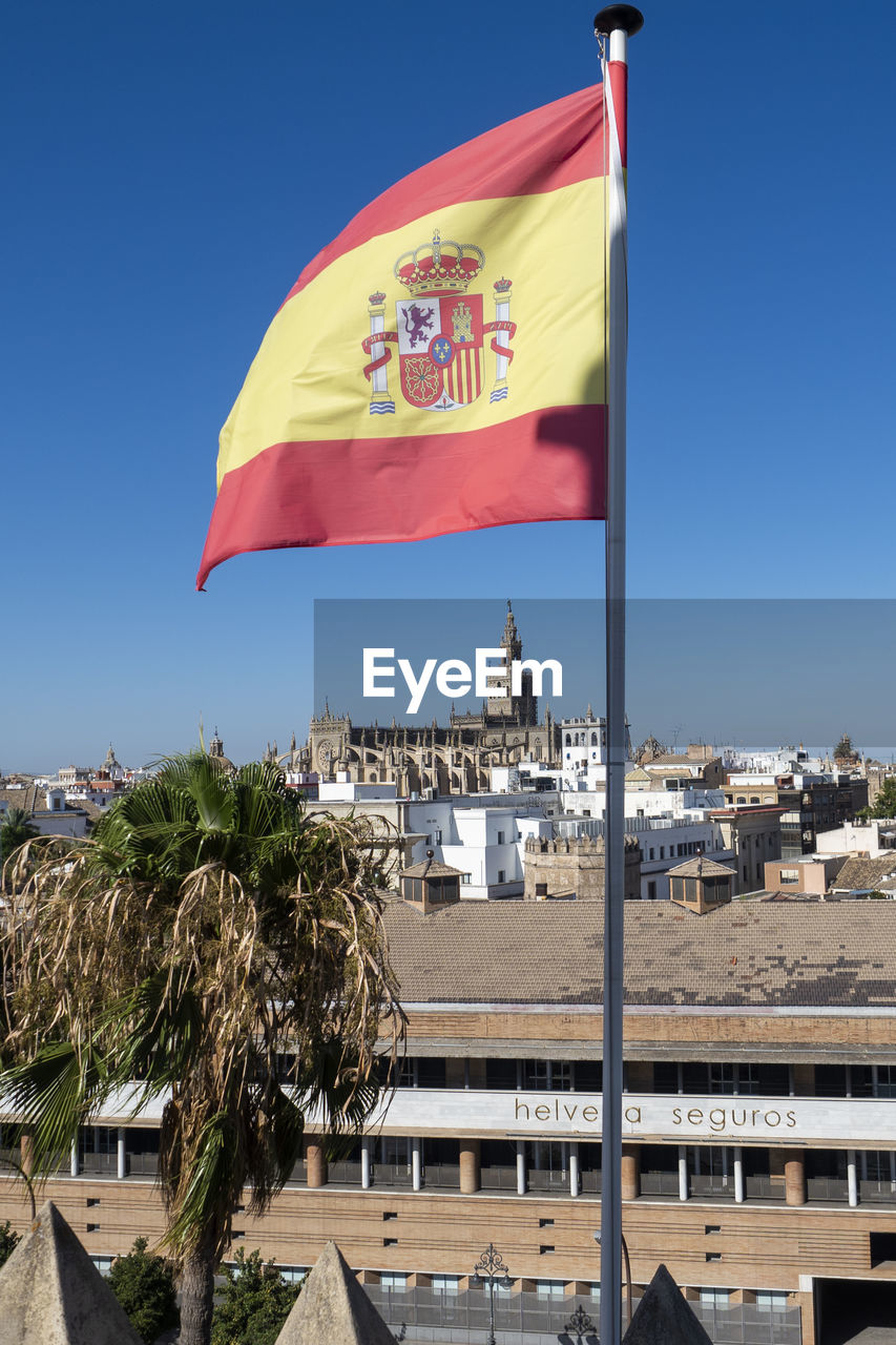 Flag against buildings in city against clear blue sky